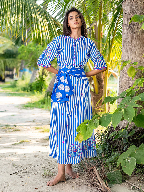 Woman in a blue and white striped dress standing in a tropical setting with palm trees.