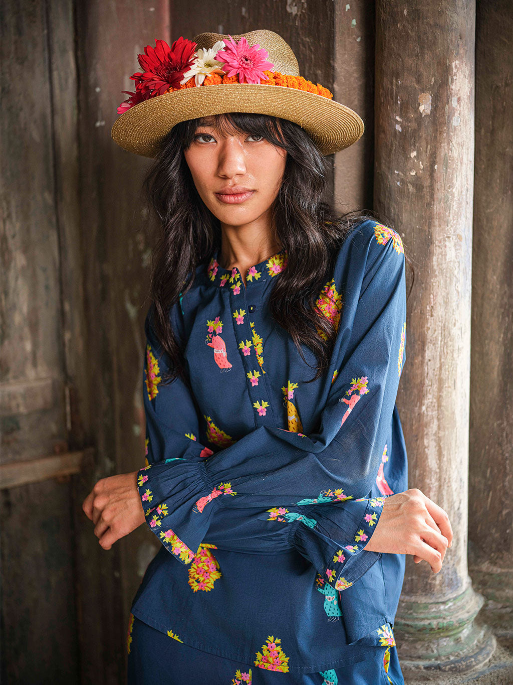 Woman wearing a floral hat and blue tunic blouse with colorful patterns in an outdoor setting.