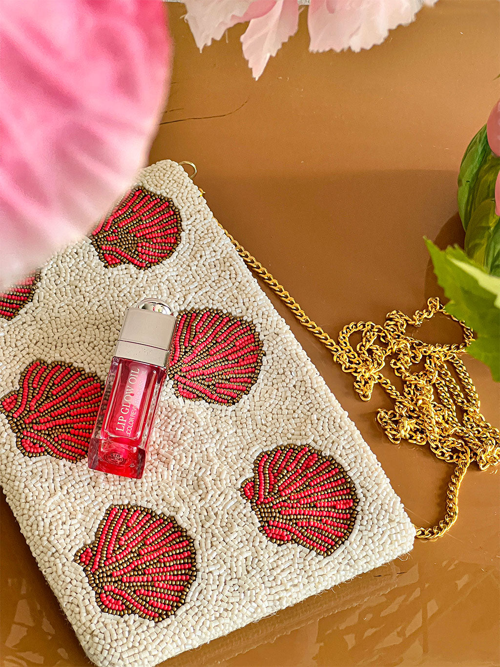 Handcrafted white seed bead shoulder bag with six coral and pink seashell designs on neutral background