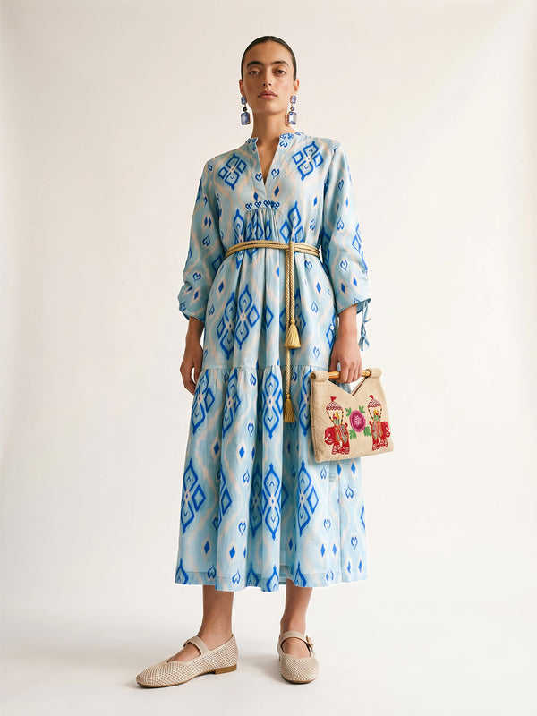Woman styling the light blue Catmint Ikat dress with a belt and a bamboo handle bag.