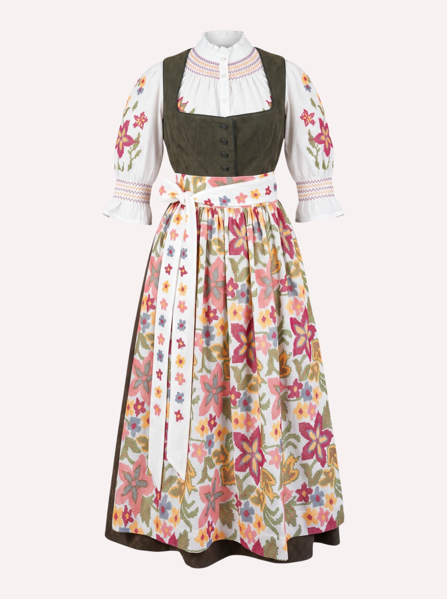 Nimo x Münchner Manufaktur dirndl apron with dense red and green floral cross-stitch embroidery styled over a loden green dirndl.