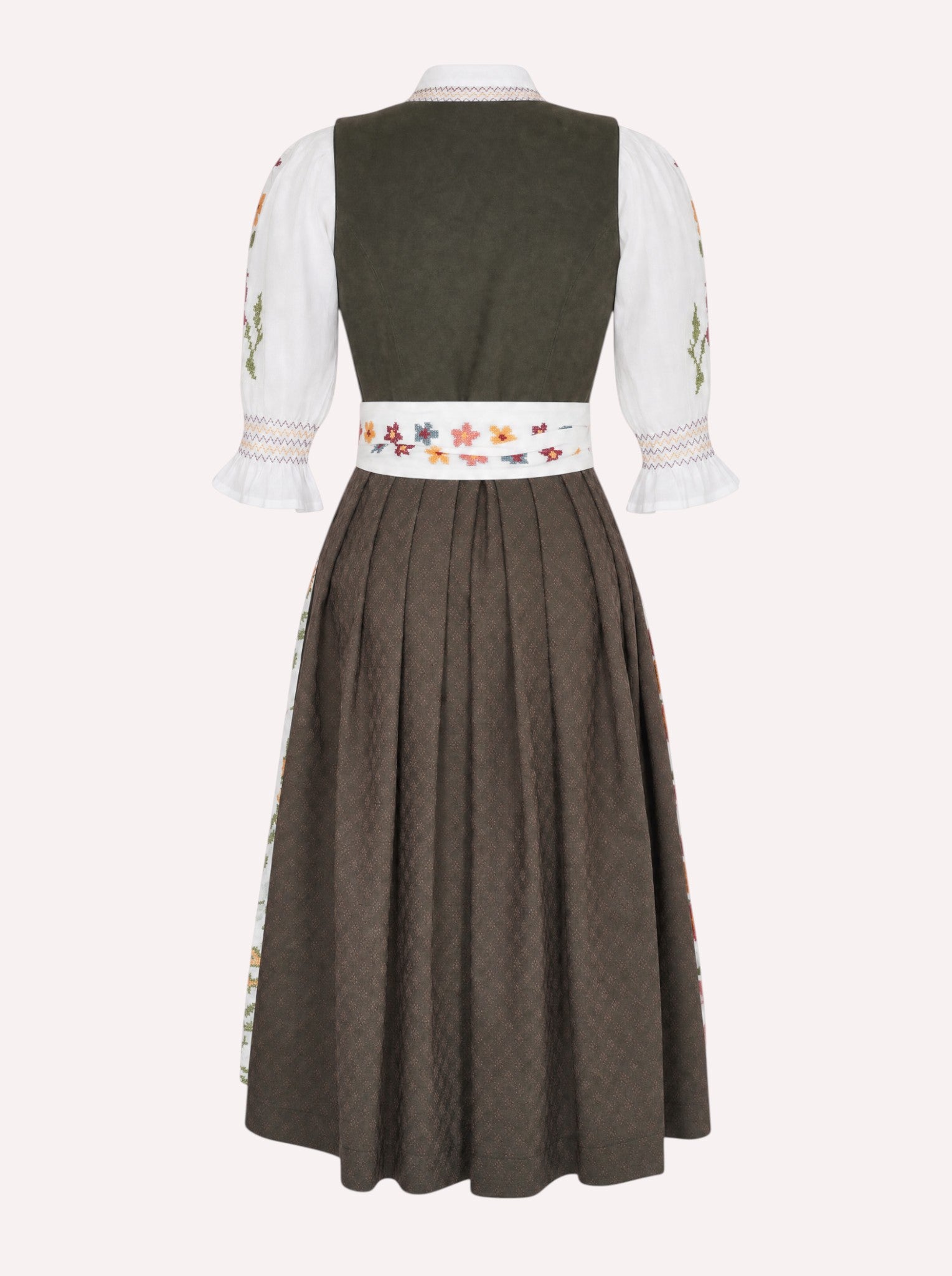 Nimo x Münchner Manufaktur dirndl apron with dense green and red floral cross-stitch embroidery from back, styled over a dark green dirndl.