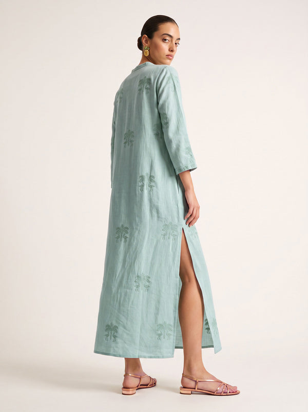 A woman modeling a long, mint green kaftan with a high side slit, shown from a three-quarter back angle against a plain light beige studio background.