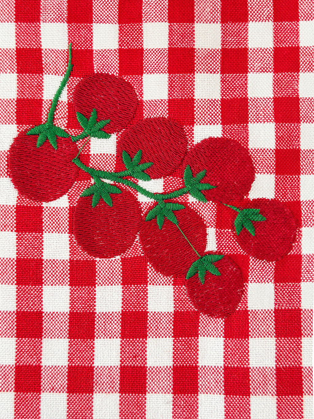 Close-up of intricate hand-guided embroidery on a premium red and white checkered organic cotton fabric.